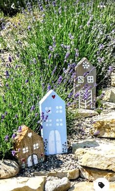 two small houses sitting on top of rocks in front of lavenders and grass with purple flowers