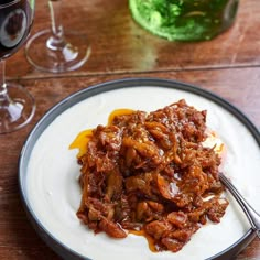 a white plate topped with meat and sauce next to two wine glasses on a wooden table