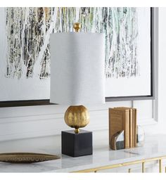 a gold lamp sitting on top of a white table next to a painting and books