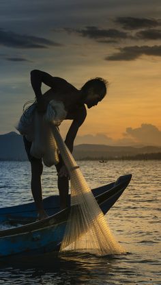 a man standing on top of a blue boat holding a net in his hand as the sun sets