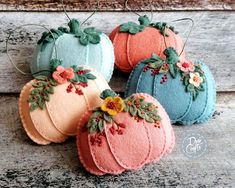 four felt pumpkins sitting on top of a wooden table with leaves and flowers painted on them