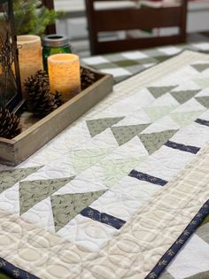 a quilted table runner with pine cones and candles