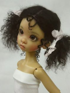 a close up of a doll wearing a white dress with black hair and big eyes