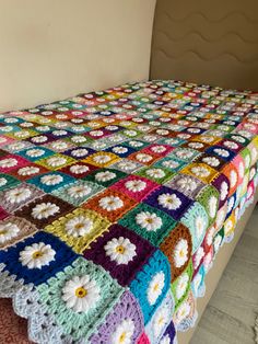 a multicolored crocheted blanket on top of a bed with white flowers