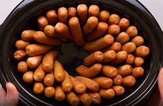 a person holding a black bowl filled with hot dogs