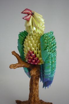 a colorful bird sculpture sitting on top of a wooden tree branch in front of a gray background