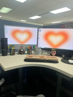 an office cubicle with two computer monitors and a heart - shaped keyboard on the desk