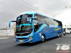 a large blue bus driving down a street next to tall buildings and power lines on a cloudy day