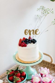 a cake and cupcakes on a wicker table with one written in gold