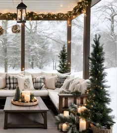 a covered porch with christmas decorations and candles on the table, surrounded by evergreens