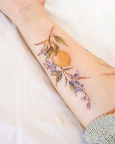 a woman's arm with flowers and an orange on it