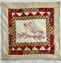 a red and white quilted wall hanging with a bird on it's side