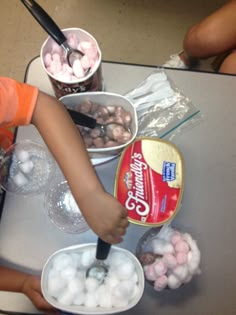 two children are making marshmallows at a table with plastic cups and spoons