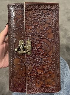 a person holding up a brown leather book with an ornate design on the front cover