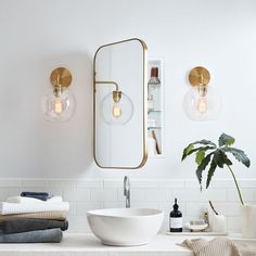 a white bathroom with gold fixtures and lights on the wall, along with a large mirror