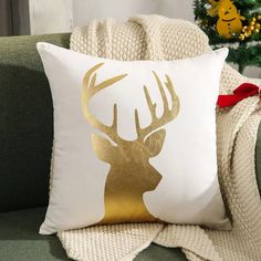 a white and gold deer pillow sitting on top of a green couch next to a christmas tree