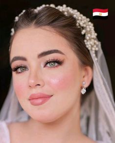 a woman wearing a veil with pearls on top of her head and makeup in the background