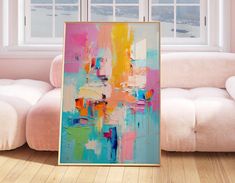 an abstract painting is displayed in front of a white couch and window with pink walls