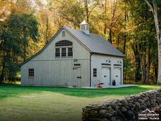 a white barn in the middle of a forest with trees around it and a stone wall