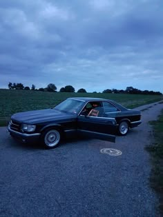 a black car parked on the side of a road next to a field at night