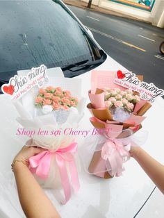 two bouquets of flowers are sitting on the hood of a white car with pink ribbon