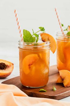 two mason jars filled with peaches and garnished with mint on a cutting board