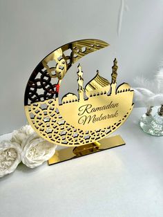 a gold and black ramadan mubarak decoration on a white table with flowers