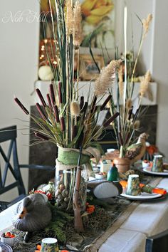 the table is set with dishes, cups and vases filled with dried flowers on it