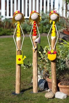 three wooden poles with painted figures on them in the grass next to potted plants