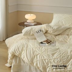 a bed with white comforter and pillows on top of it next to a lamp