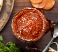 a jar filled with sauce sitting on top of a table next to vegetables and crackers