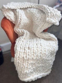 a white knitted blanket sitting on top of an orange chair