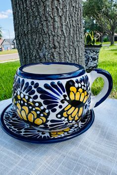 a blue and yellow coffee cup sitting on top of a table next to a tree