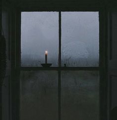 a candle sitting on top of a window sill in front of a rain covered window