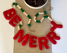 the word merry spelled out in red and green beads next to a bowl of pine cones