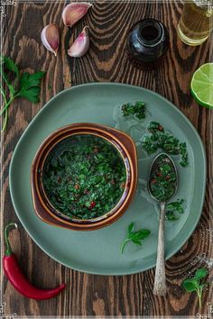 a green plate topped with a bowl of soup next to two spoons and pepper