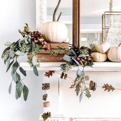 a mantel with white pumpkins and greenery on it