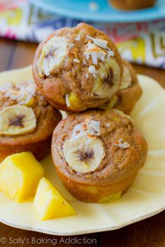 three banana muffins on a white plate with pineapple and coconut wedges