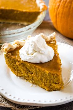 a slice of pumpkin pie on a plate with whipped cream and an orange in the background