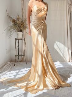 a woman in a gold dress standing on a white sheeted floor with her back turned to the camera