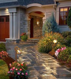 a house that is lit up at night with flowers in the front yard and landscaping around it