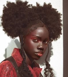 a woman with dark skin and red makeup is standing in front of a white wall