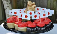 cupcakes with red frosting and white flags on them are displayed in front of a gold statue