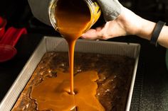 someone pouring caramel sauce on top of a brownie in a baking pan,