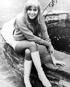 a woman sitting on top of a stone wall next to a water fountain wearing knee high boots