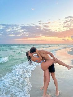 a man and woman kissing on the beach with waves crashing in front of them at sunset