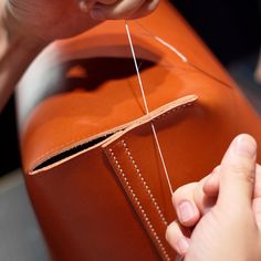 someone is stitching something on the back of a leather bag with scissors and thread