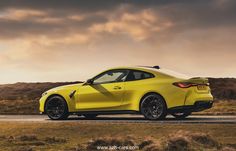 a yellow sports car is driving down the road with dark clouds in the sky behind it