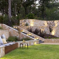 an outdoor living area with stone walls and seating on the grass, surrounded by trees