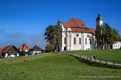 a large white church sitting in the middle of a lush green field next to trees